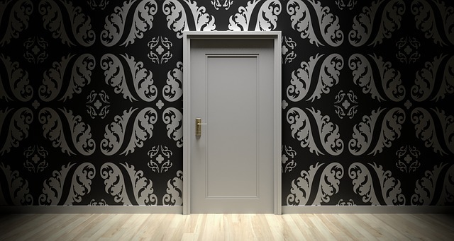 Photograph of a wall with black and white decorative wallpaper and a white door, which is shut, in the center of the wall.